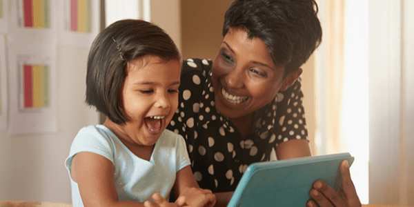 A mother laughing with a girl using a tablet