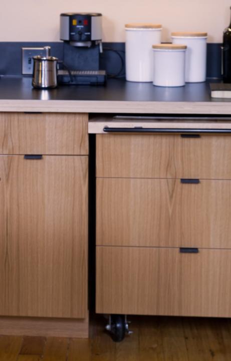 Photo of kitchen with trolley on wheels that fits under bench with coffee machine and white kitchen containers on top.