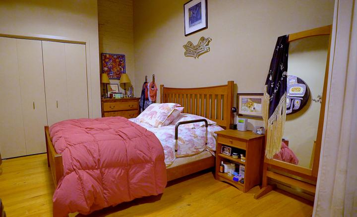 Photo of bedroom with bed placed in middle of room with a pink duvet with support rail on side.