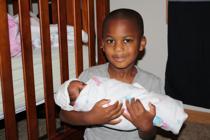 Big brother holding baby siter who is wrapped in a swaddle and wearing a hat