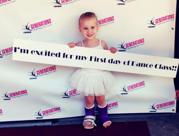 Photo of 4 year old Taryn waering splints on both of her legs holding a sign at her dance recital