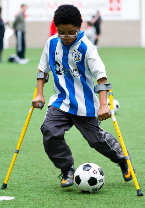 Image of teenage boy using crutches kicking a soccer ball.