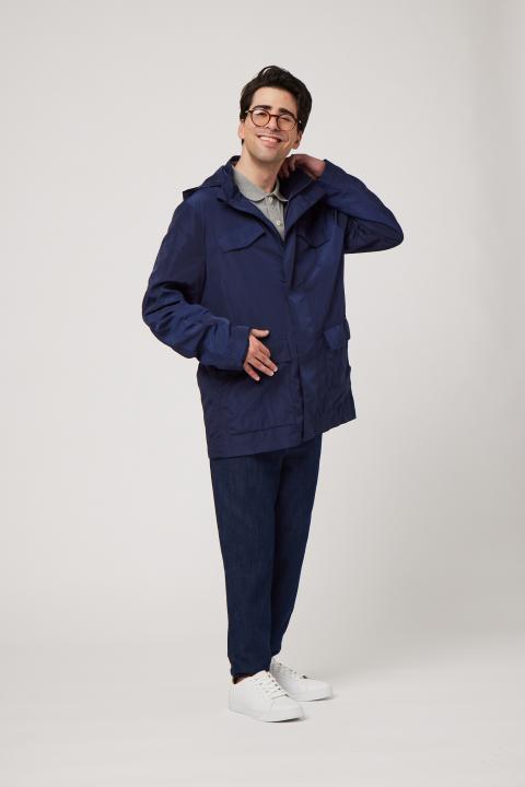 Man with dark hair and glasses wearing a navy blue raincoat and dark pants