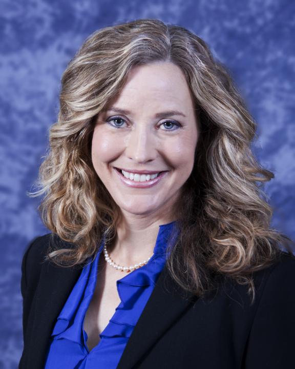 Researcher Noelle Moreau wearing a black blazer with a blue shirt over a blue background