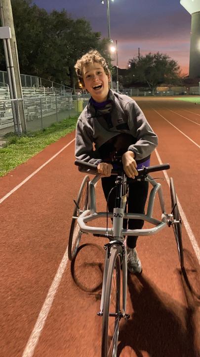 A teenager in a black jacket is using a frame runner to run around a track