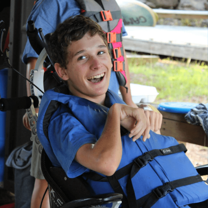 Young man sitting in a wheelchair smiling while wearing a life vest