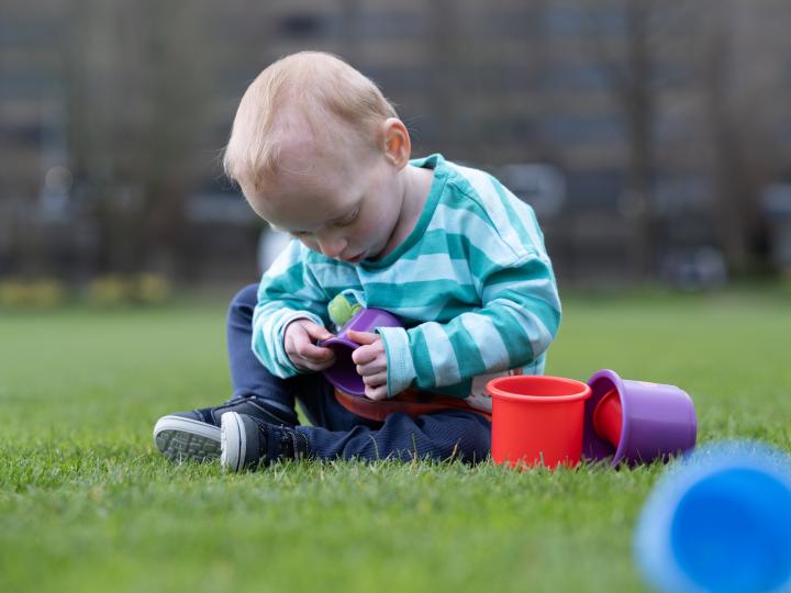 Baby sitting on the grass and playing with multicolored cups