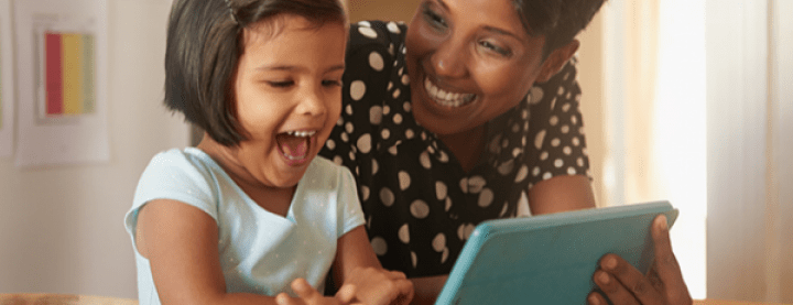 A mother laughing with a girl using a tablet