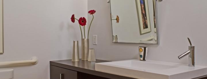 Photo of bathroom sink with access for wheelchair as well as low mirror that is tilted 