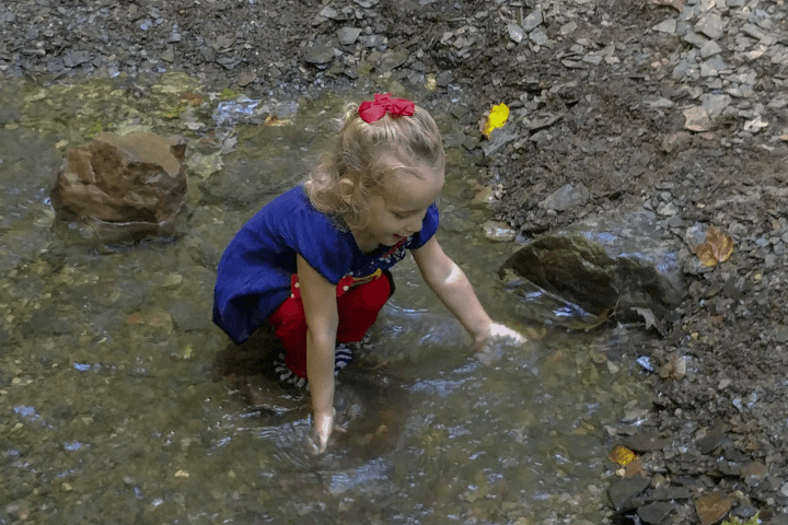 Taryn (4 years old) kneeling down in a creek and feelings the water.