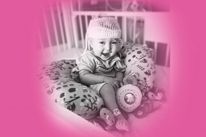 Owen sitting up smiling in crib at the hospital with neonatal baby monitor on his head