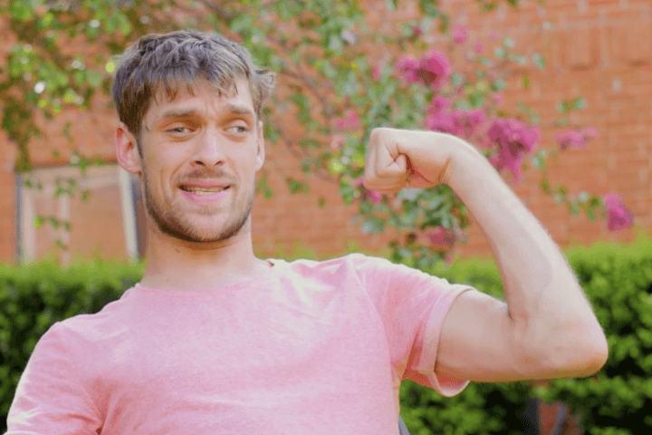 Zach Anner outside in salmon shirt, flexing his arm