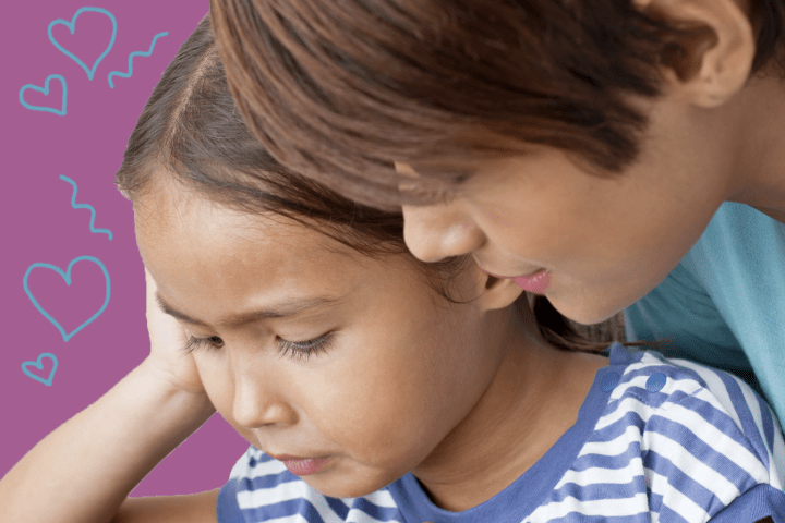 Mother standing over her daughter while they look at something together.