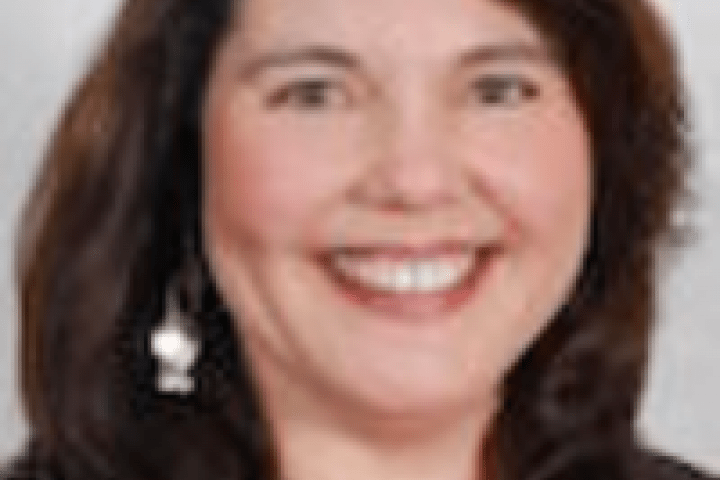 Photo of Mary Ganotti in a red shirt with a black sport coat on a grey background