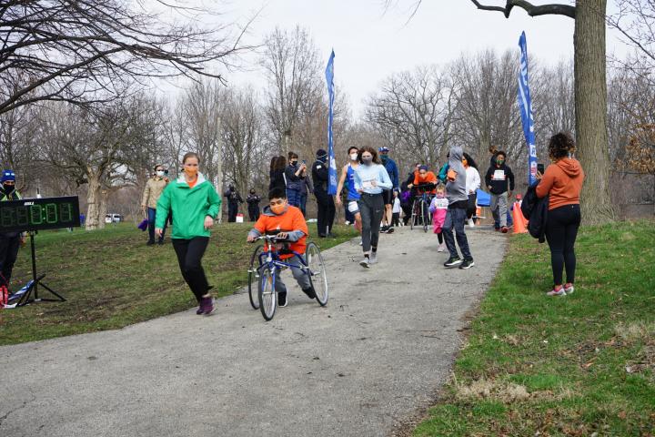 Woman in green shirt and black pants running next to a young boy in an orange shirt in a frame runner