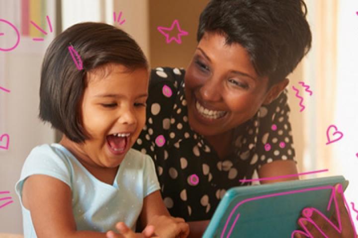 Young girl and woman smiling while looking at a tablet