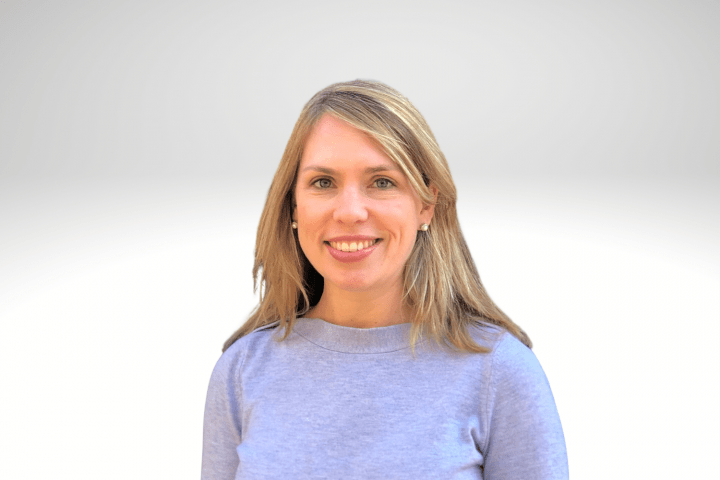 Kristen has long blond hair and is smiling wearing a blue sweater