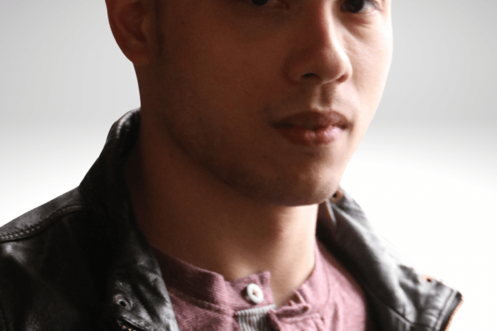 Peter has dark brown hair, he is gazing into the camera with a serious expression on his face, wearing a leather jacket