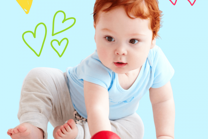 A little baby boy with bright red hair is sitting and playing with a red ball