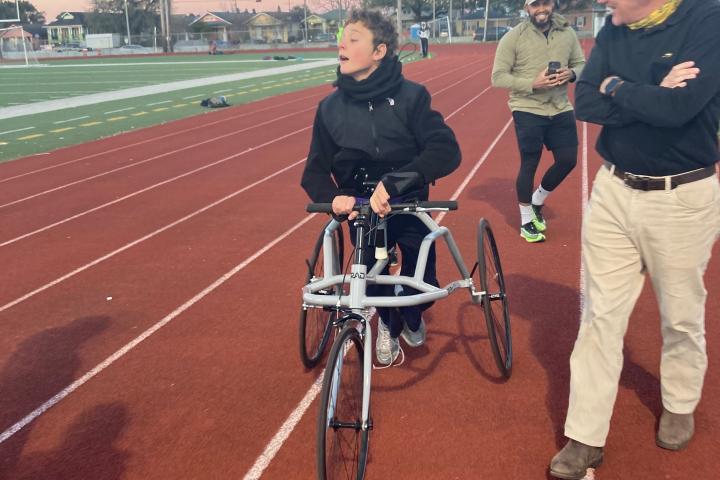 A teenager in a black jacket is using a frame runner to run around a track