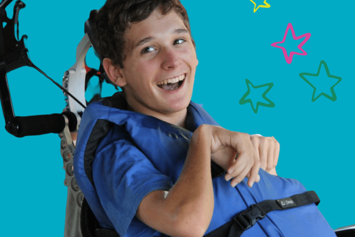 Young man sitting in a wheelchair smiling while wearing a life vest
