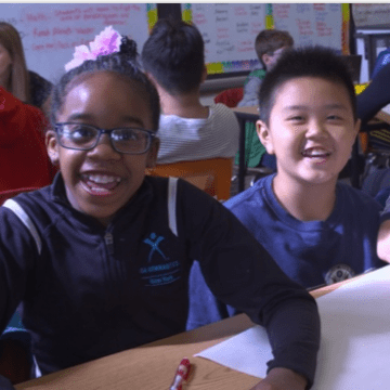 Two students sitting in a classroom at a desk smiling directly at camera