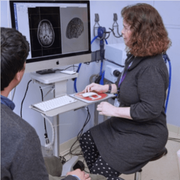 Researcher Kathleen Friel sitting in front of a computer reviewing a black and white image of the brain