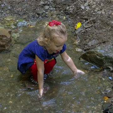 Taryn (4 years old) kneeling down in a creek and feelings the water.