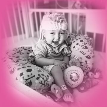 Owen sitting up smiling in crib at the hospital with neonatal baby monitor on his head