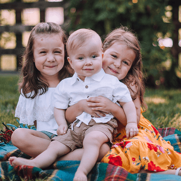Three siblings sitting on a rug with Owen (Age 1) who has CP sitting in the middle
