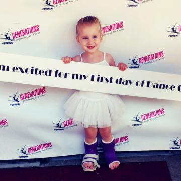 Photo of 4 year old Taryn waering splints on both of her legs holding a sign at her dance recital