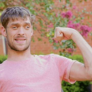 Zach Anner outside in salmon shirt, flexing his arm