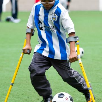 Image of teenage boy using crutches kicking a soccer ball.