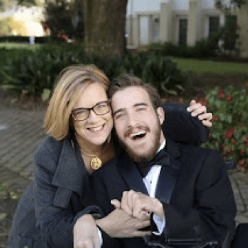 Woman in a grey sweater hugging a man in a tuxedo who is sitting in a wheelchair