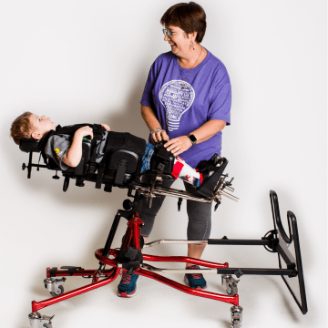 Ginny wearing a purple shirt smiling with a little boy lying in a red stander 