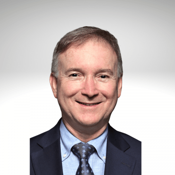 Paulo Selber has short greyish brown hair and is smiling wearing a blue shirt, tie and blue blazer.