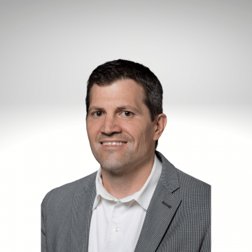 Christopher Modleski has dark hair and is smiling wearing a white button down and grey blazer
