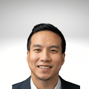 Byron Lai has dark hair and is smiling. He is wearing a white shirt with a dark jacket.