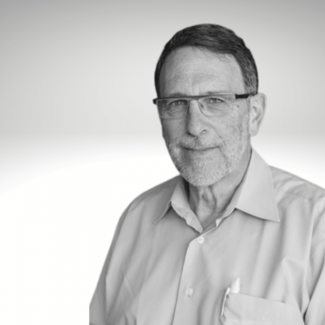 Peter Rosenbaum has dark hair, glasses and a short grey beard. He is wearing a white button down shirt.