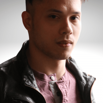 Peter has dark brown hair, he is gazing into the camera with a serious expression on his face, wearing a leather jacket