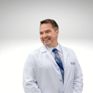 Michael Kruer has short brown hair, he is smiling wearing a lab coat with a blue tie