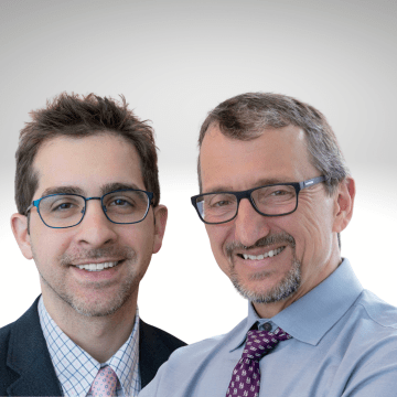 Dr. Georgiadis on left with short dark hair and glass wearing a pink tie, blue shirt and dark jacket, next to Dr. Novachek with dark hair and glassed wearing a blue shirt and maroon tie.