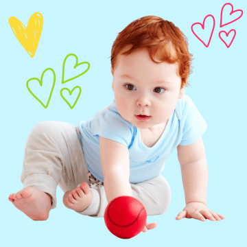 A little baby boy with bright red hair is sitting and playing with a red ball