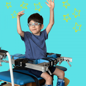 A boy wearing blue shorts and a blue shirt is sitting on a bench with his hands up in the air reaching for stars!