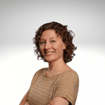 Dr. Heather Riordan has curley shoulder length light brown hair. She is wearing a tan short sleaved shirt and is smiling.