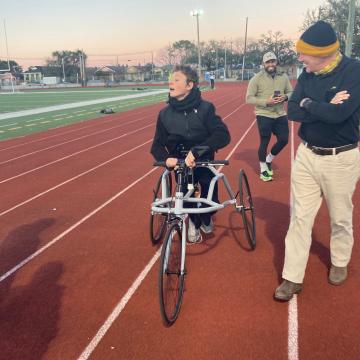 A teenager in a black jacket is using a frame runner to run around a track