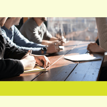 Image of people sitting at a table taking notes with a pencil and paper