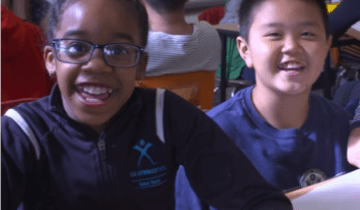 Two students sitting in a classroom at a desk smiling directly at camera
