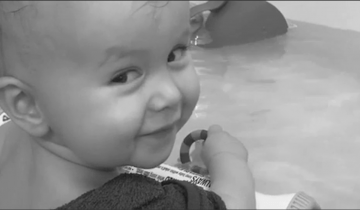 Owen age 1 years old smiling looking behind his shoulder in the bath playing with a toy