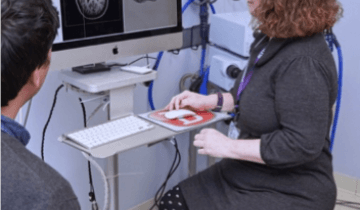 Researcher Kathleen Friel sitting in front of a computer reviewing a black and white image of the brain